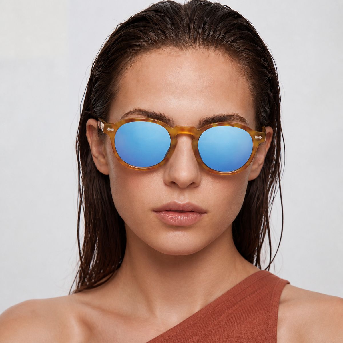 Modelo femenina con lentes Solivo SIA Carey Celeste, montura carey y lentes celestes, retrato frontal con top terracota.